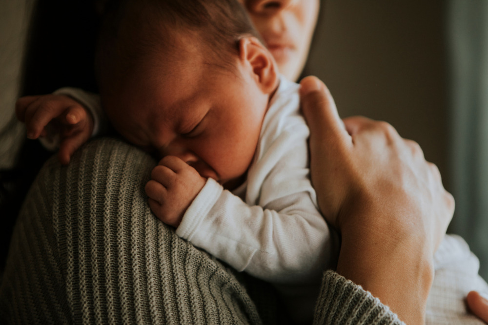 Close-up image of a sleeping baby, being held by its mother against her shoulder.