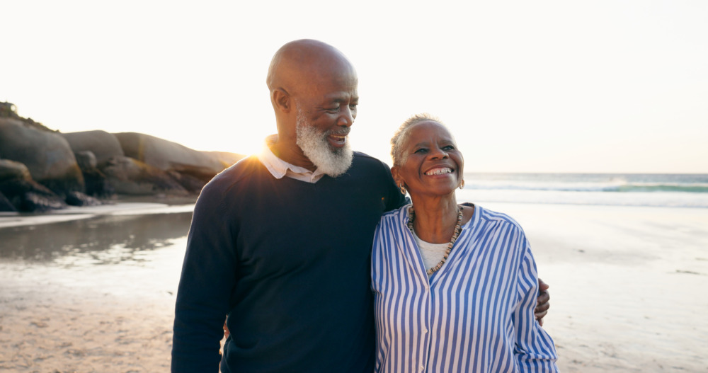 Senior couple smiling and hugging on the beach.