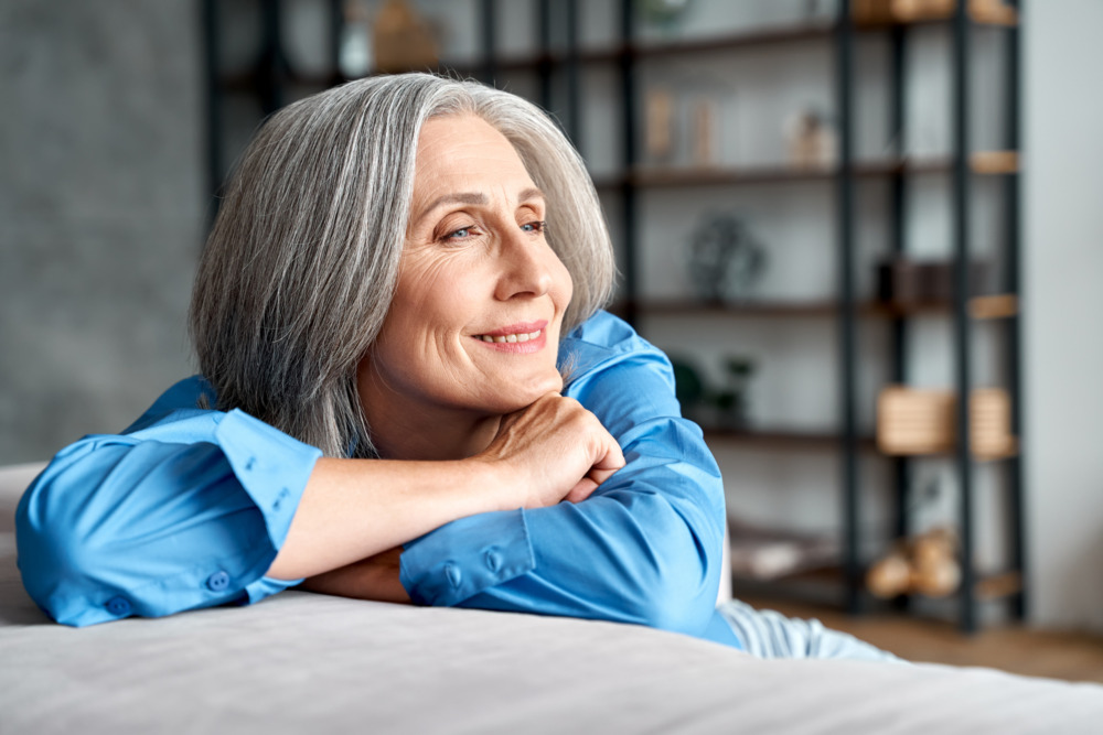 Senior woman sat in her living room, smiling and looking peaceful.