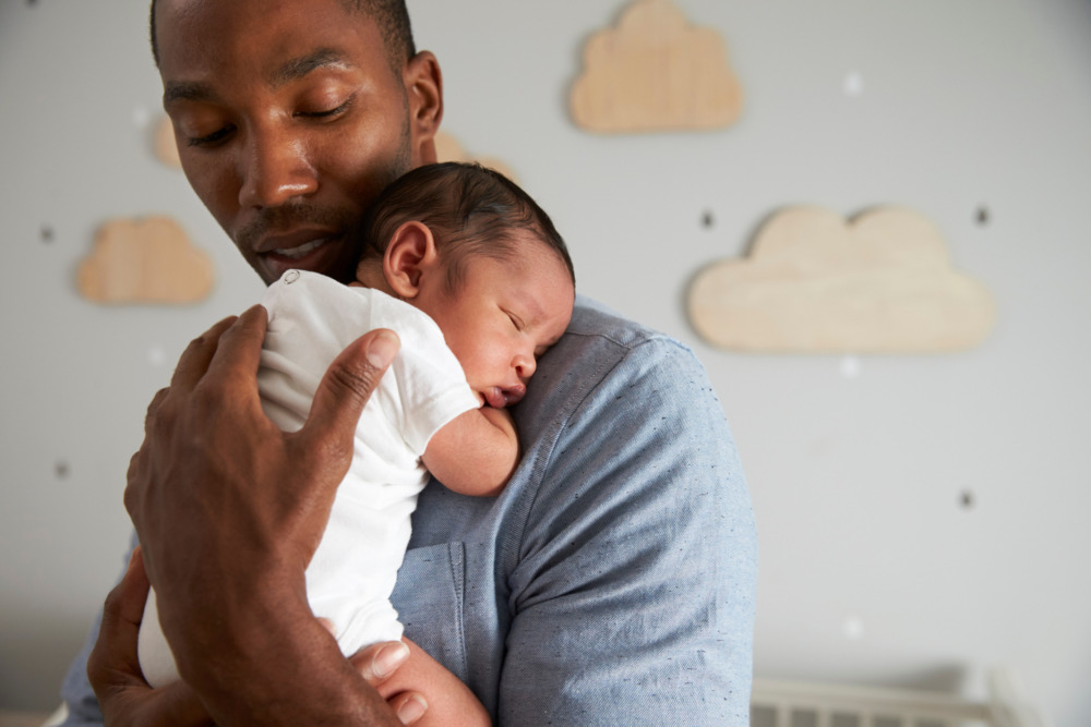 Father holding his newborn son against his chest in a nursery.