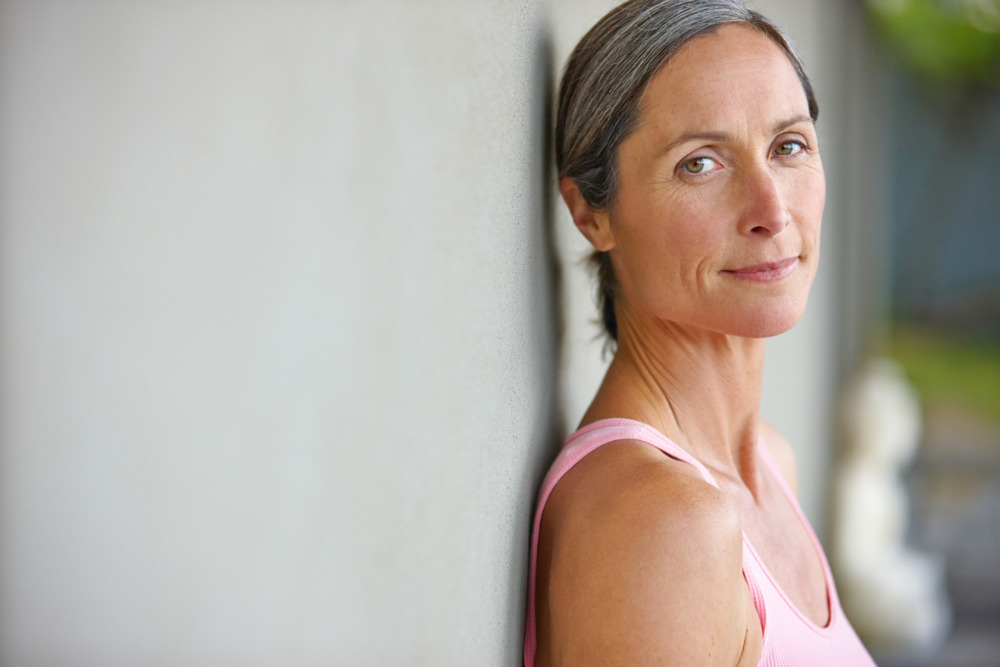 Image of a woman leaning against a wall wearing gym clothes, and looking at the camera.