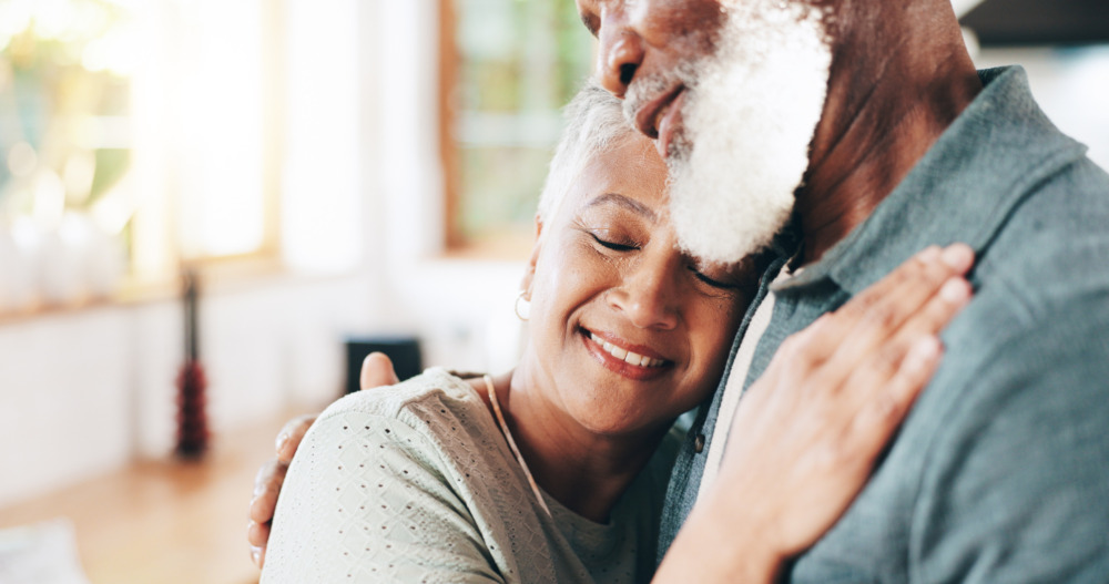 Close up of a senior woman, resting her head on her husband's chest.