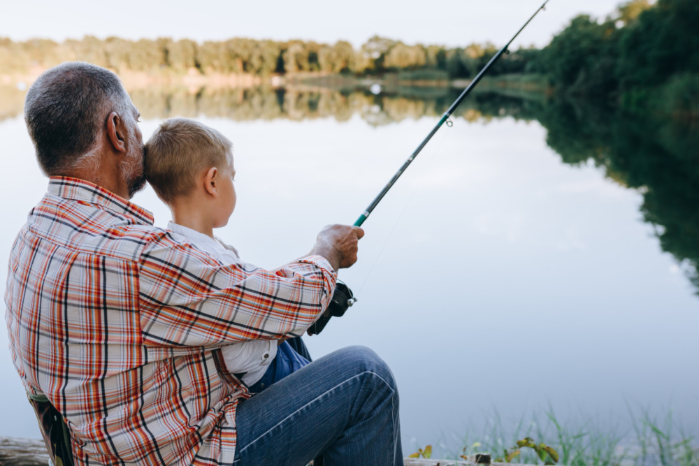 A young boy fishing with his grandfather on a lake.