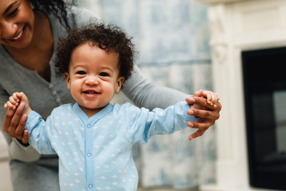 A young child learning to walk, with support from his mother holding his hands.