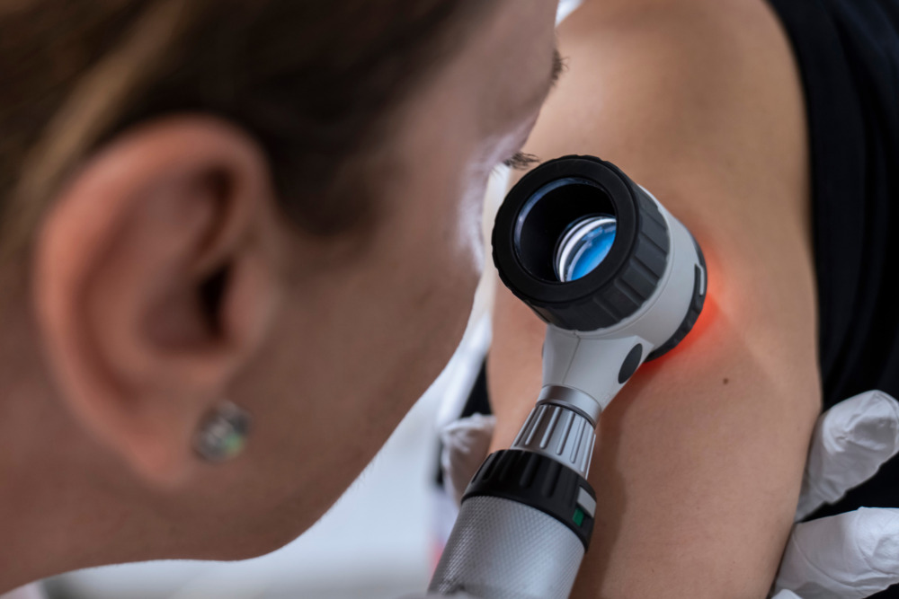 A dermatologist inspects their patient's skin with a microscope.